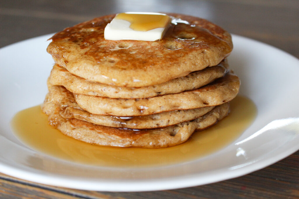 stack of sourdough gingerbread pancakes topped with butter and maple syrup on a plate
