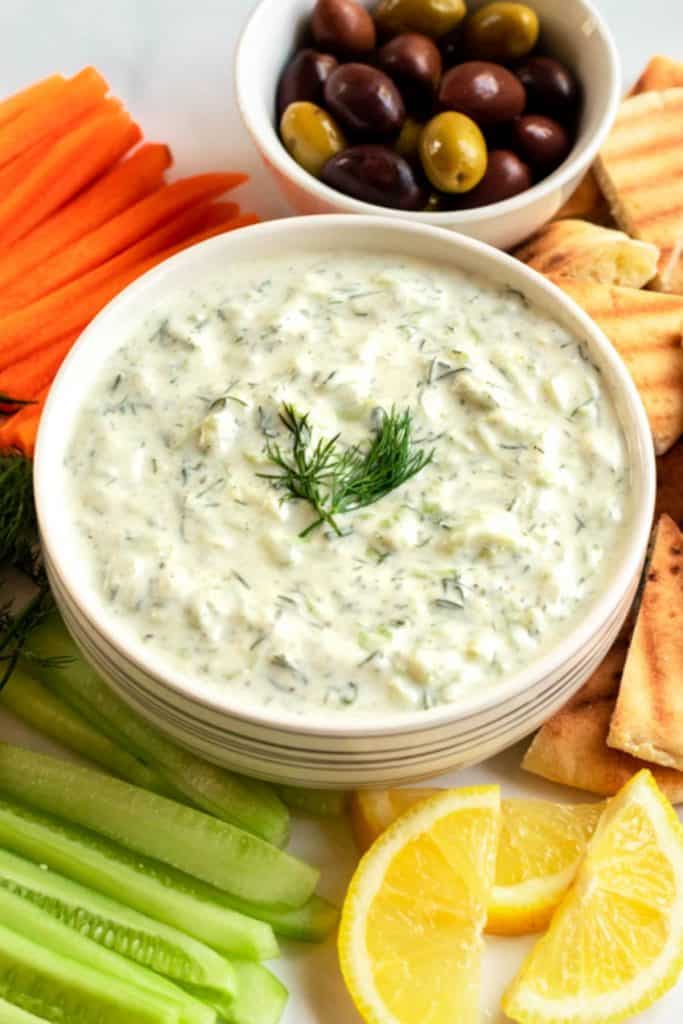 tzatziki sauce topped with fresh dill with carrots and olives and cucumbers and lemons on the side