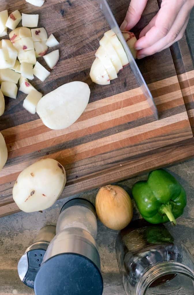 slicing red potatoes on wooden cutting board with ingredients surrounding