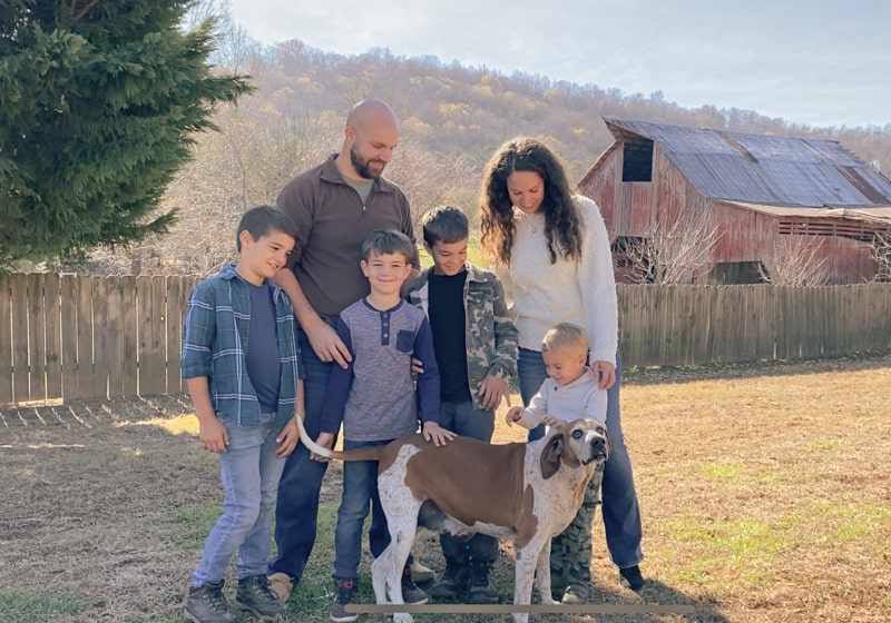 homesteading family with hound dog in front of barn