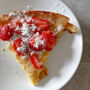 slice of sourdough dutch baby topped with strawberries and powdered sugar