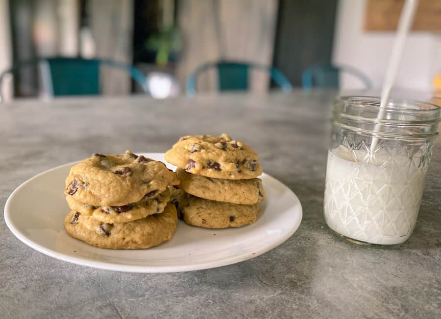 sourdough einkorn chocolate chip cookies stacked on plate with glass of milk being poured