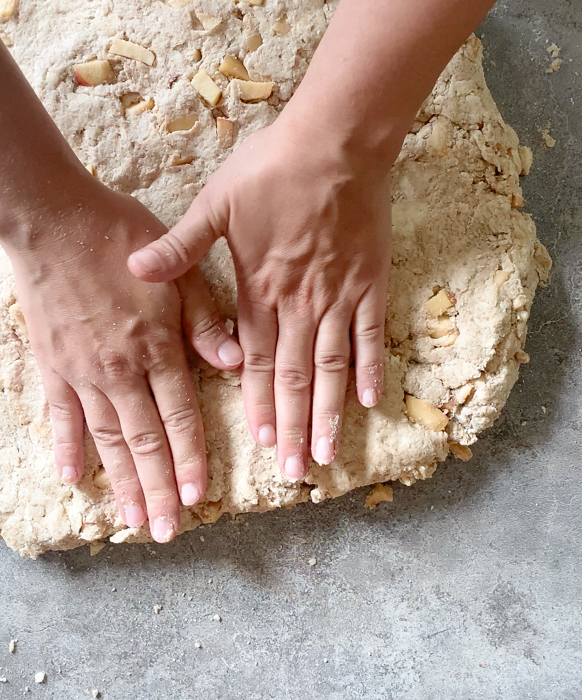 A woman's hands pressing apple cinnamon sourdough scone dough into a circle.