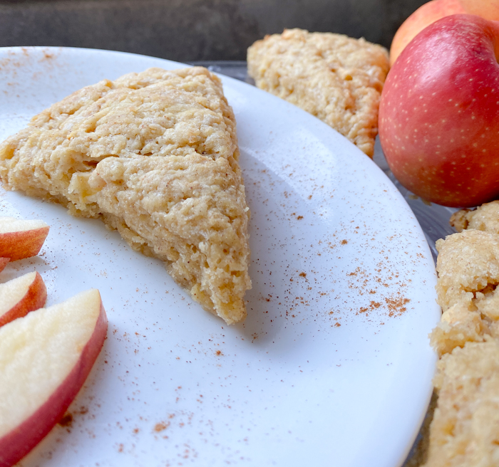 A sourdough einkorn scone on a white plate surrounded by apples.