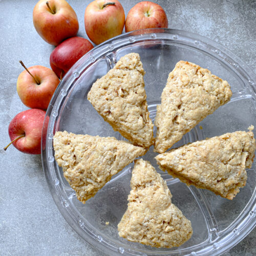 apple cinnamon sourdough einkorn scones on glass dish. the scones are surrounded by whole red apples.