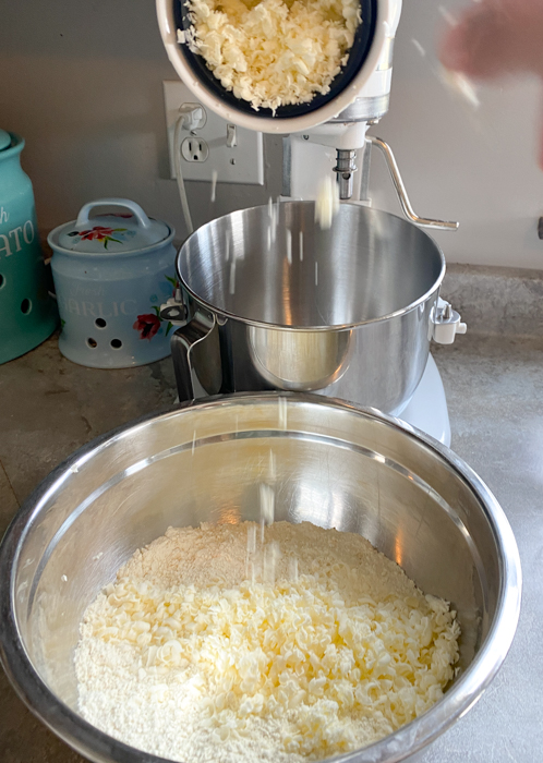 Kitchenaid mixer with grater attachment grating butter into a bowl of scone dough.