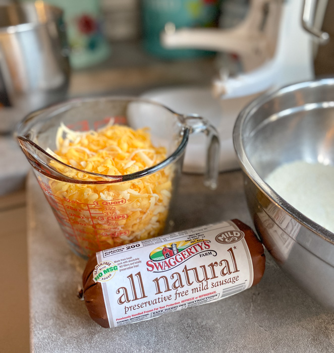 Shredded cheese in a measuring cup and a roll of uncooked breakfast sausage on a countertop.