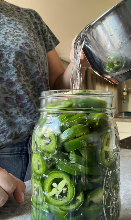 Pouring brine into a jar filled with jalapeños for fermented jalapeño peppers.