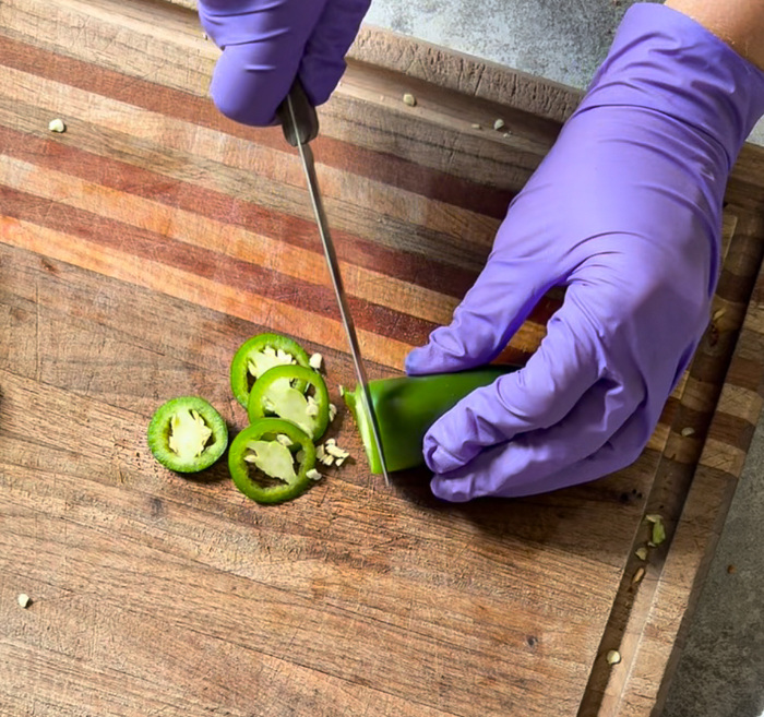 Gloved hands slicing a jalapeño
